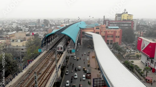 Electric rapid public transport in Delhi, India, Vehicles moves along delhi metro railroad and passes by Delhi city buildings & skyscrapers, now Indian urban mass transit metro railway system.