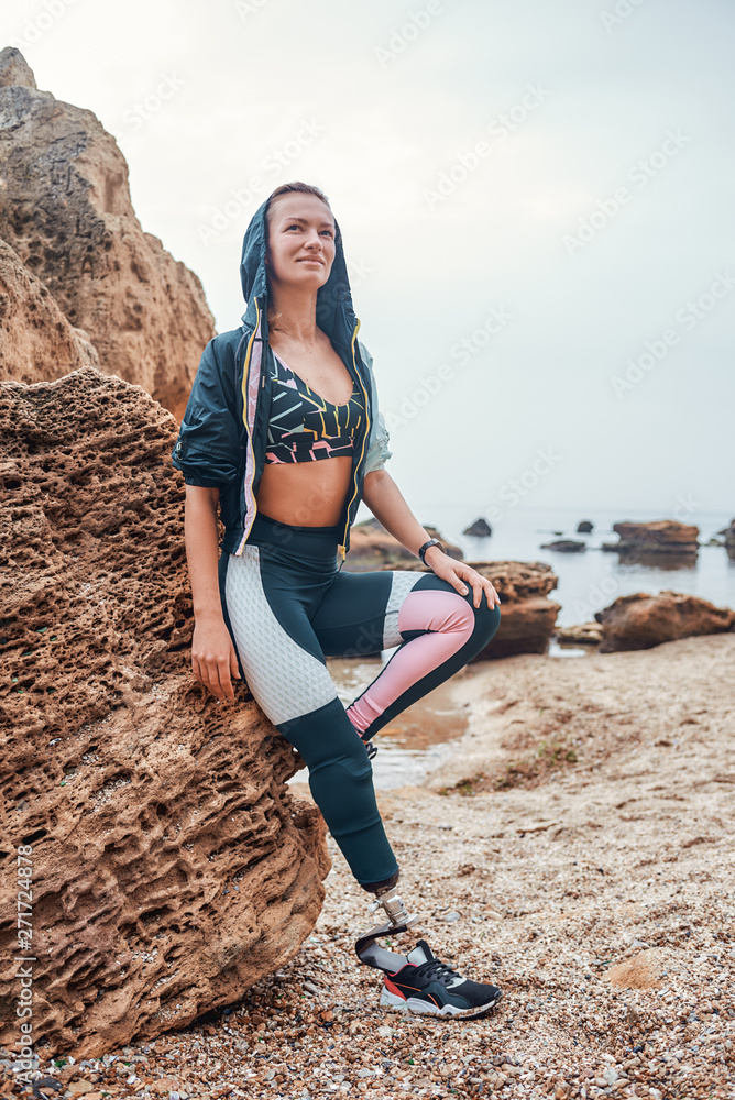 Challenging my body. Full length of young positive disabled woman with prosthetic  leg in sports clothing standing on the beach after morning workout Stock  Photo | Adobe Stock