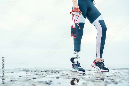 Doing my best. Cropped image of disabled woman in sports clothing with prosthetic leg holding skipping rope while standing in front of the sea.