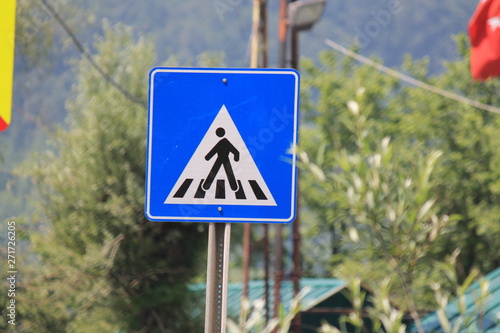 A blue pedestrian crossing sign against a background of green tree