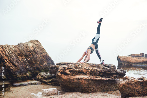 Yoga in the morning. Healthy and sporty disabled athlete woman in sportswear with prosthetic leg standing doing yoga on the stone in front of the sea.