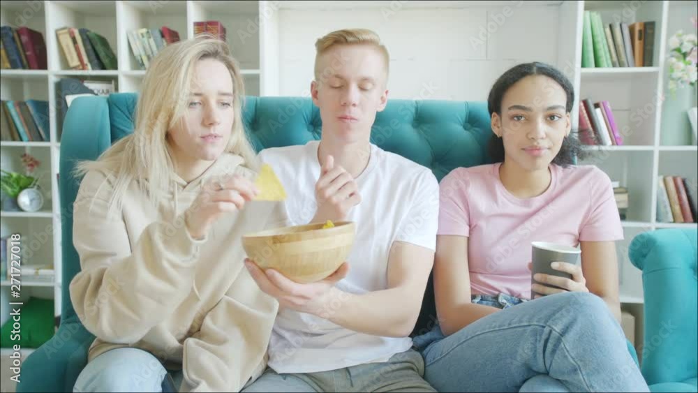 Happy three friends are watching TV and eating snacks together in the sofa Happy three friends are watching TV and eating snacks together in the sofa