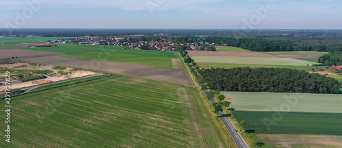 Aerial photo taken from high altitude with drone, flat landscape with meadows and fields, small town in the background, sand pit at the edge, with country road and forest, drone shot