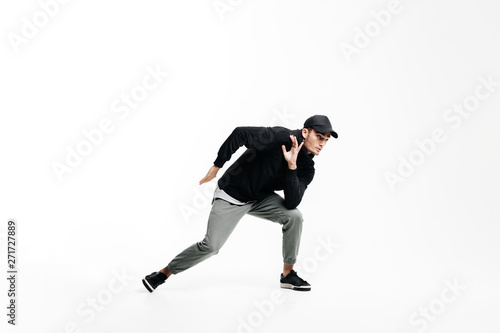 Handsome young man wearing a black sweatshirt, gray pants and a cap dancing street dances on a white background