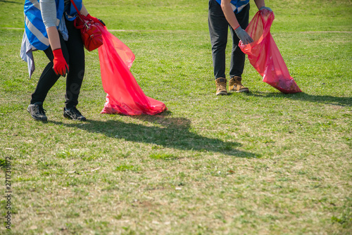 Man and woman volunteer wearing picking up trash and plastic waste in public park. Young people wearing gloves and putting litter into red plastic bags outdoors