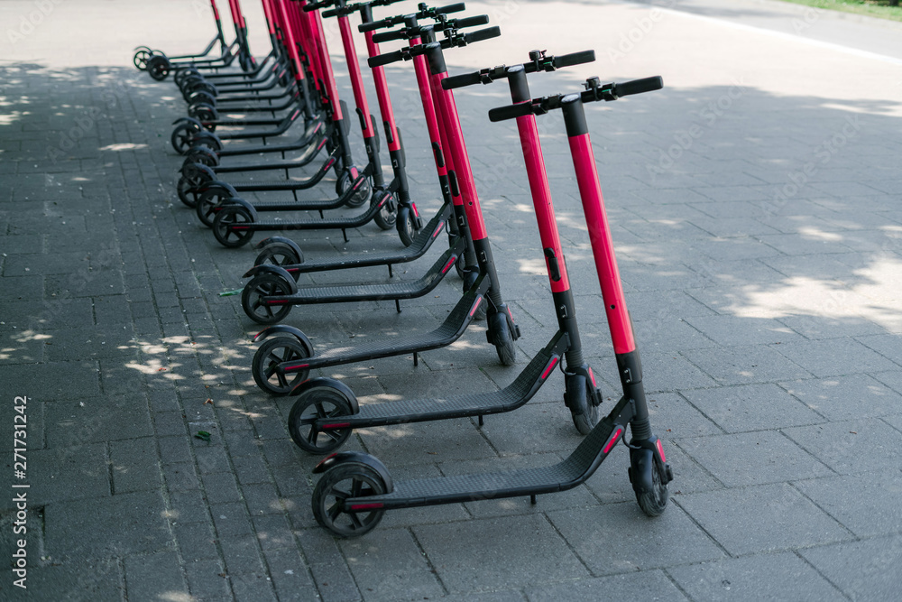 Modern eco electric city scooters for rent outdoors on the sidewalk. Alternative tourism, transportation around the city, bike replacement service. E-scooters can be rented with an app Modern eco electric city scooters for rent outdoors on the sidewalk. Alternative tourism, transportation around the city, bike replacement service. E-scooters can be rented with an app