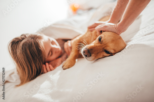 Mother and daughter petting dog lying in the bed