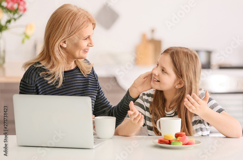 Mature woman and her cute granddaughter drinking tea in kitchen