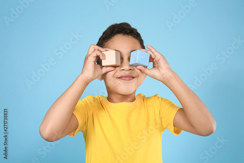 Portrait of cute little boy with cubes on color background © Pixel-Shot