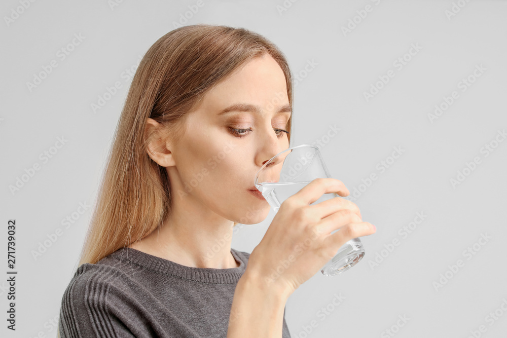 Beautiful young woman drinking water on light background Beautiful young woman drinking water on light background
