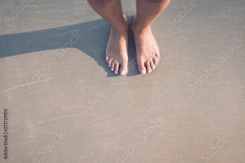 two female feet stay on the sand.