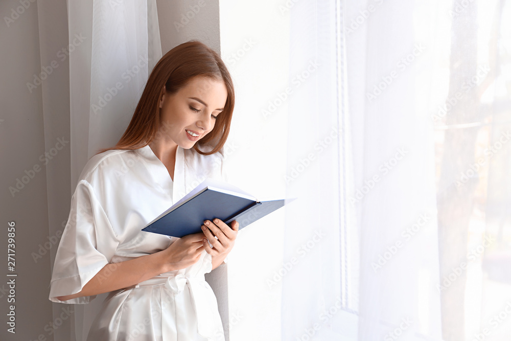 Beautiful young woman reading book near window Beautiful young woman reading book near window