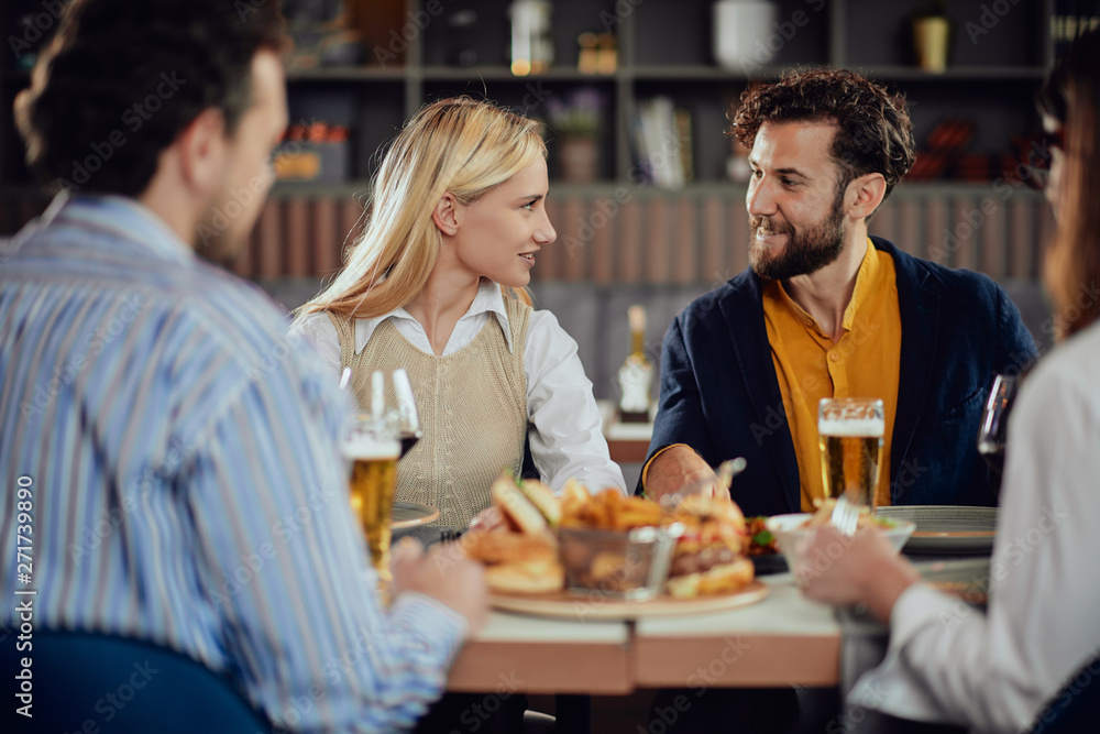 Multiethnic friends sitting at restaurant, drinking alcohol, chatting and having burgers for dinner.