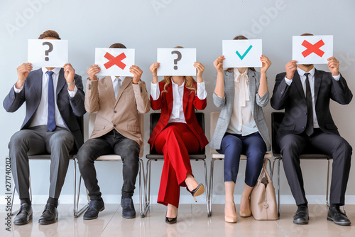 Young people holding paper sheets with different marks while sitting on chairs indoors. Job interview concept