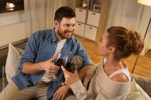 leisure, celebration and valentines day concept - happy couple drinking red wine at home in evening