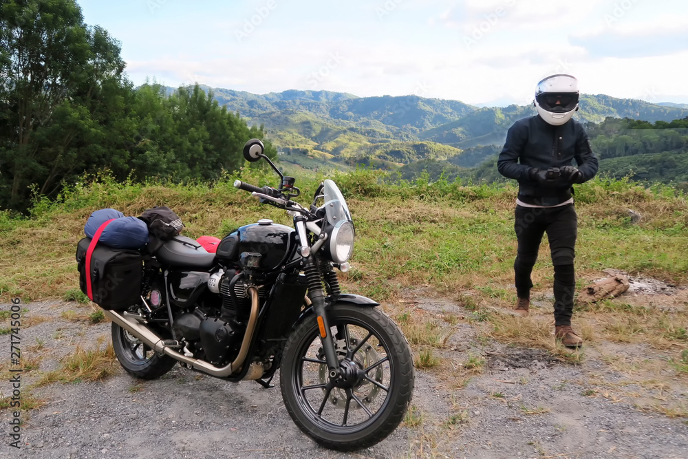 Biker walking to classic modern style motorcycle with mountain view landscape. Traveller and adventure outdoor by motorcycle concept. Biker happy in freedom lifestyle travel by motorbike.