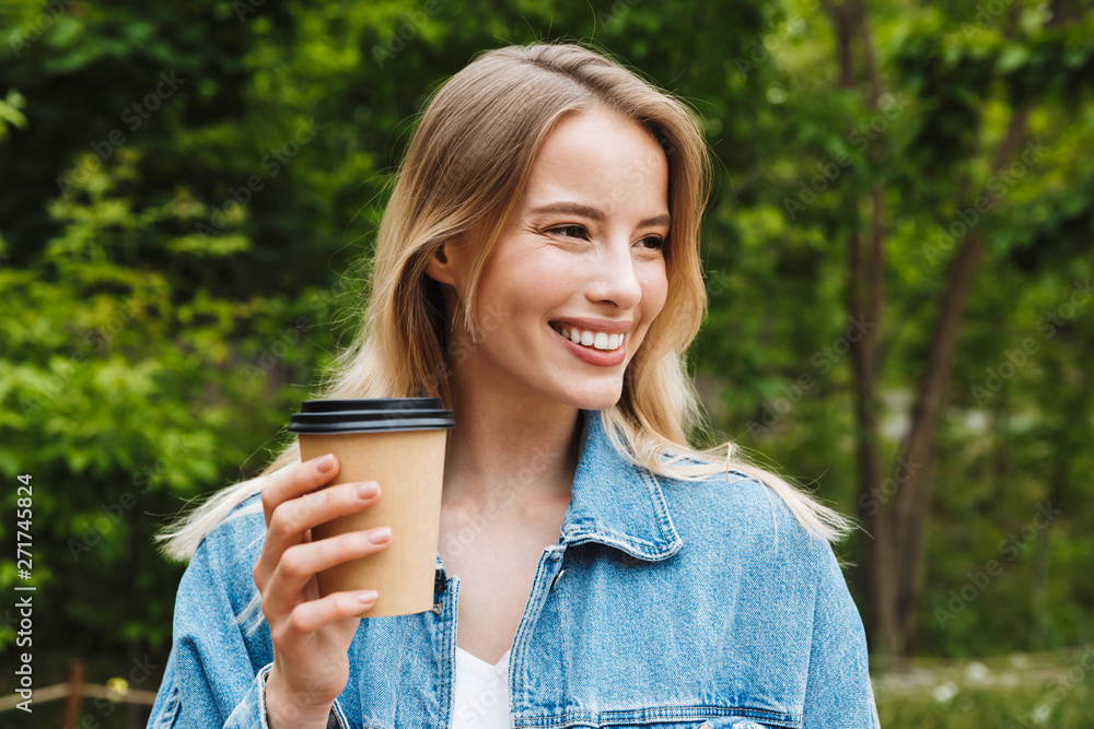 Amazing happy young woman student posing outdoors in park drinking coffee.