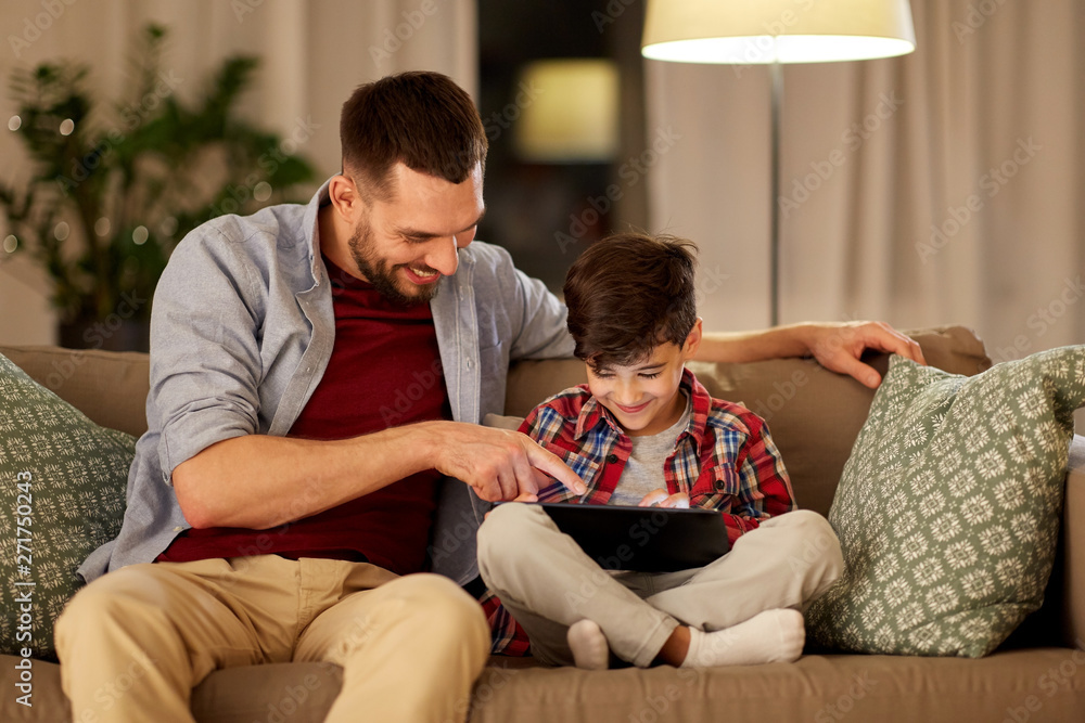 family, fatherhood, technology and people concept - happy father and little son with tablet pc computer sitting on sofa at home in evening family, fatherhood, technology and people concept - happy father and little son with tablet pc computer sitting on sofa at home in evening