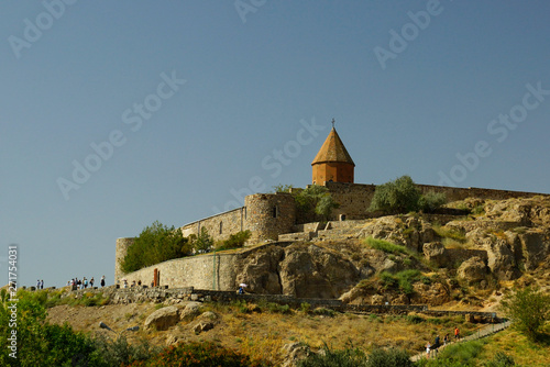 View of the central church of the Khor Virap monastery on its hill surrounded by the stone wall and tourists going on the top. Armenia.