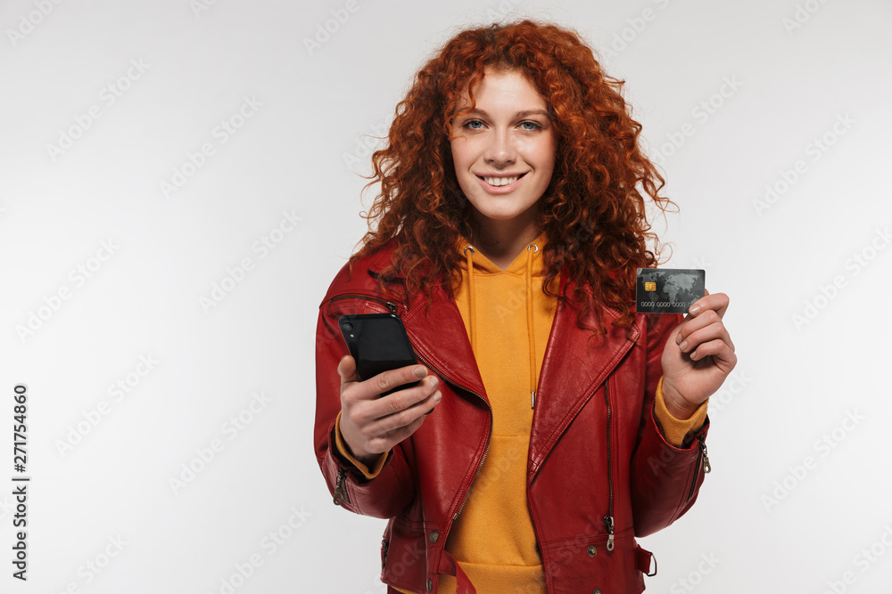 Portrait closeup of happy redhead woman 20s wearing leather jacket holding mobile phone and plastic credit card Portrait closeup of happy redhead woman 20s wearing leather jacket holding mobile phone and plastic credit card