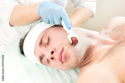 Young man on the procedure of rejuvenation and cleansing of the skin of the modern medical instrument derma roller. 
