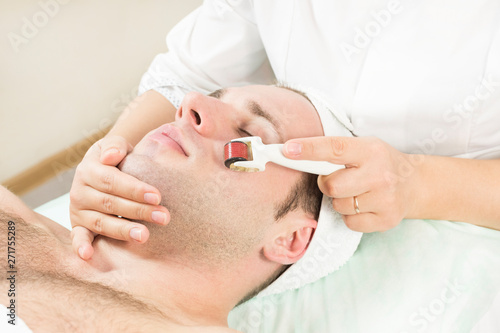 Young man on the procedure of rejuvenation and cleansing of the skin of the modern medical instrument derma roller. 