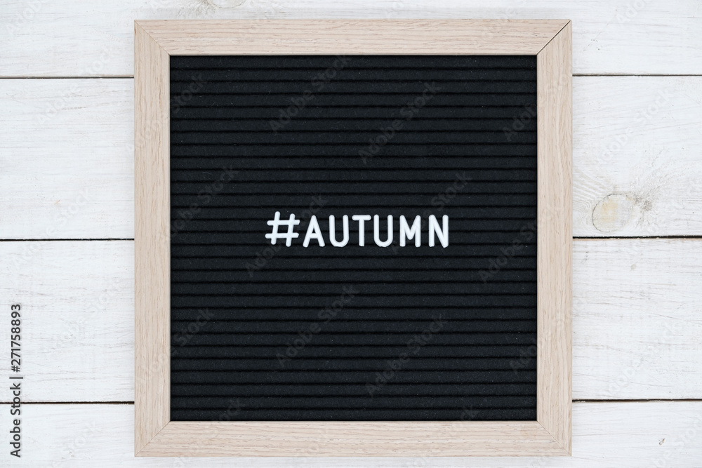 black felt Board with hashtag and word autumn in English on white wooden background