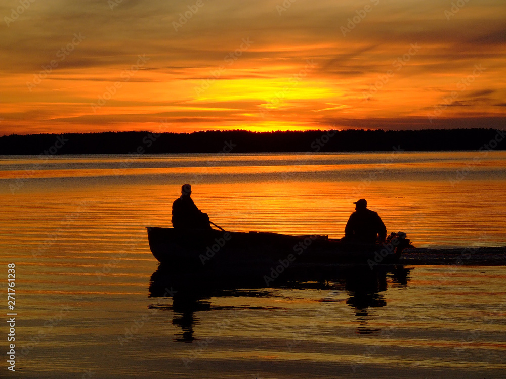 silhouettes of fishermen on a boat at sunset, floating by the shore