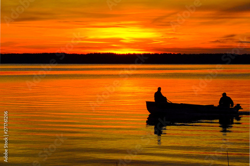 silhouettes of fishermen on a boat at sunset, floating by the shore