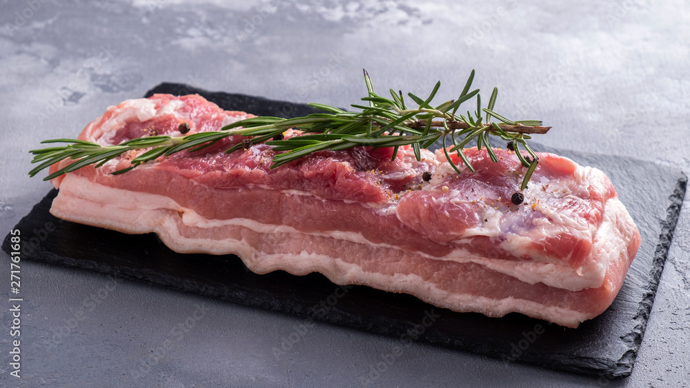 Raw pork brisket with salt, pepper and rosemary on a black stone.