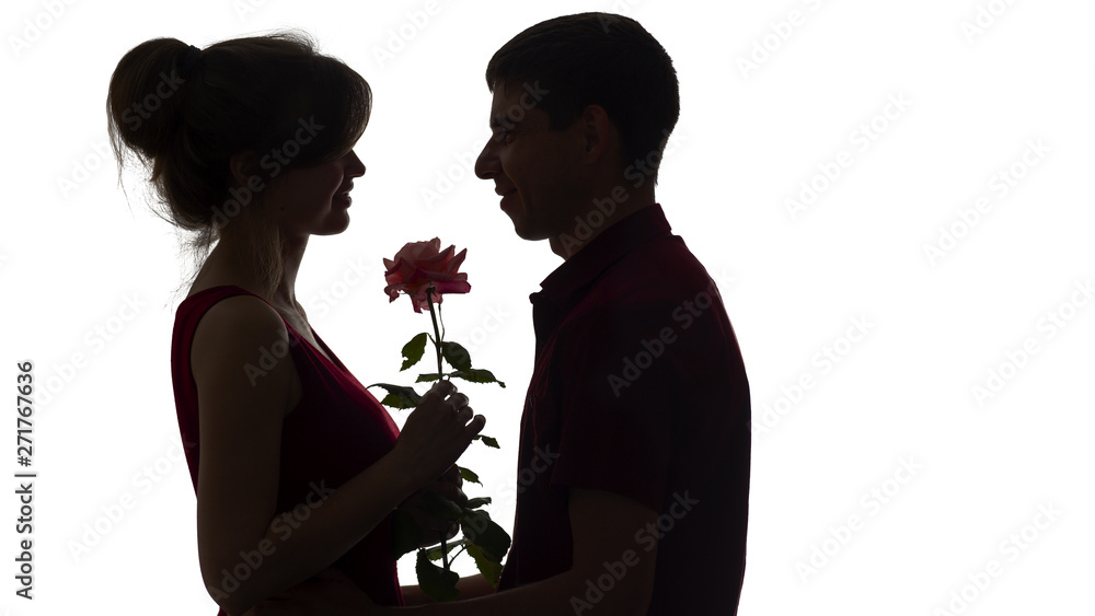 silhouette of a young couple in love on white isolated background, man gives a woman a rose flower, concept love
