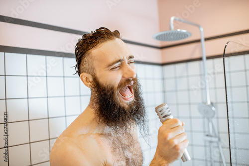 Joyful bearded man singing into the micrphone while taking a shower in the bathroom photo