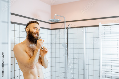 Joyful bearded man singing into the micrphone while taking a shower in the bathroom photo