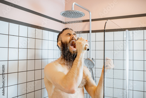 Obraz na plátně Joyful bearded man singing into the micrphone while taking a shower in the bathr