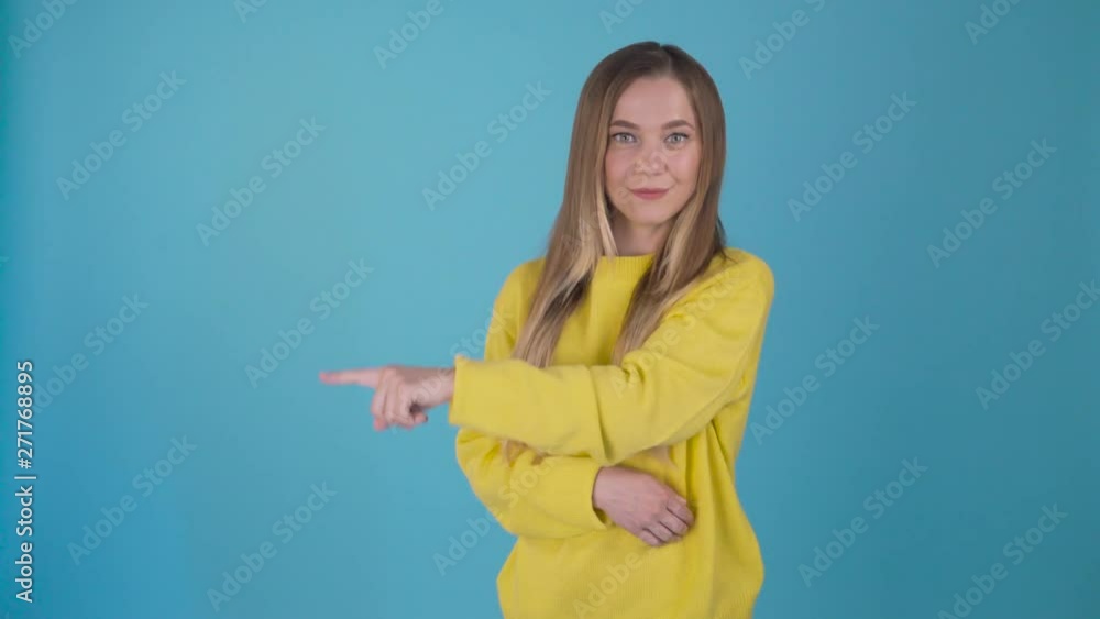 Friendly young girl shows with her index finger to the left, lowering her hand 4 times, Man on an isolated blue background. . Young student rejoices and has fun. 4K Friendly young girl shows with her index finger to the left, lowering her hand 4 times, Man on an isolated blue background. . Young student rejoices and has fun. 4K