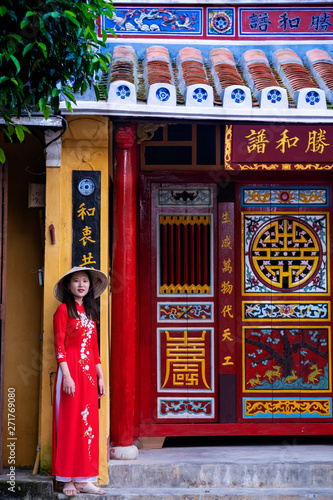 A young Vietnamese woman wearing a traditional Ao Dai dress and standing outside a temple in the historic town centre, Hoi An, Vietnam photo