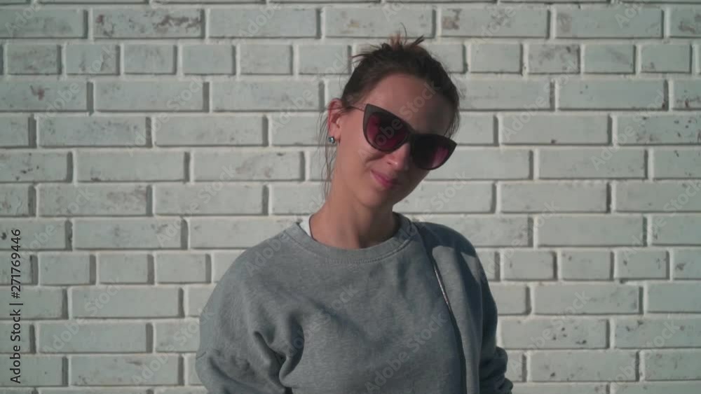 A young girl in sunglasses is looking into the camera and smiling against a white brick wall. Cute young girl looking at camera and smiling. A young girl in sunglasses is looking into the camera and smiling against a white brick wall. Cute young girl looking at camera and smiling.