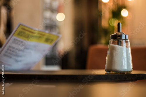 A cafe scene with a sugar shaker in the foreground and a woman holding a menu in the background.