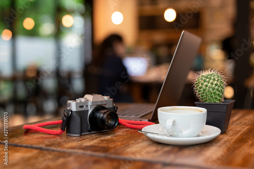 Cup of coffee and camera with laptop on wooden table.