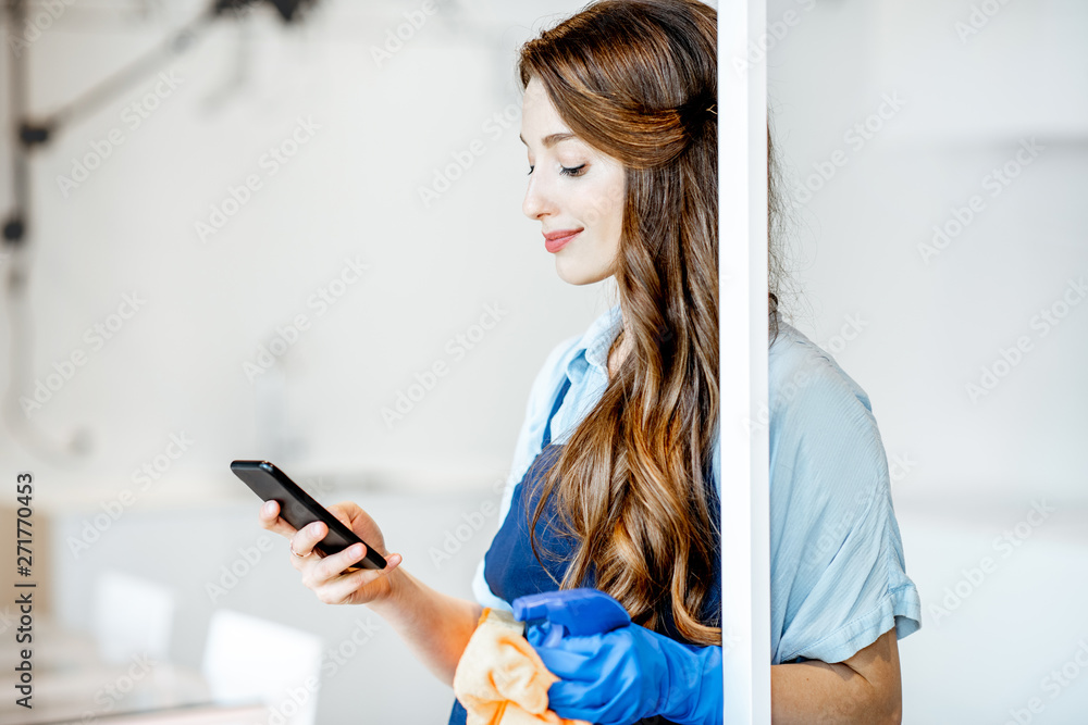 Young female housemaid using smartphone during the break after the cleaning at home Young female housemaid using smartphone during the break after the cleaning at home