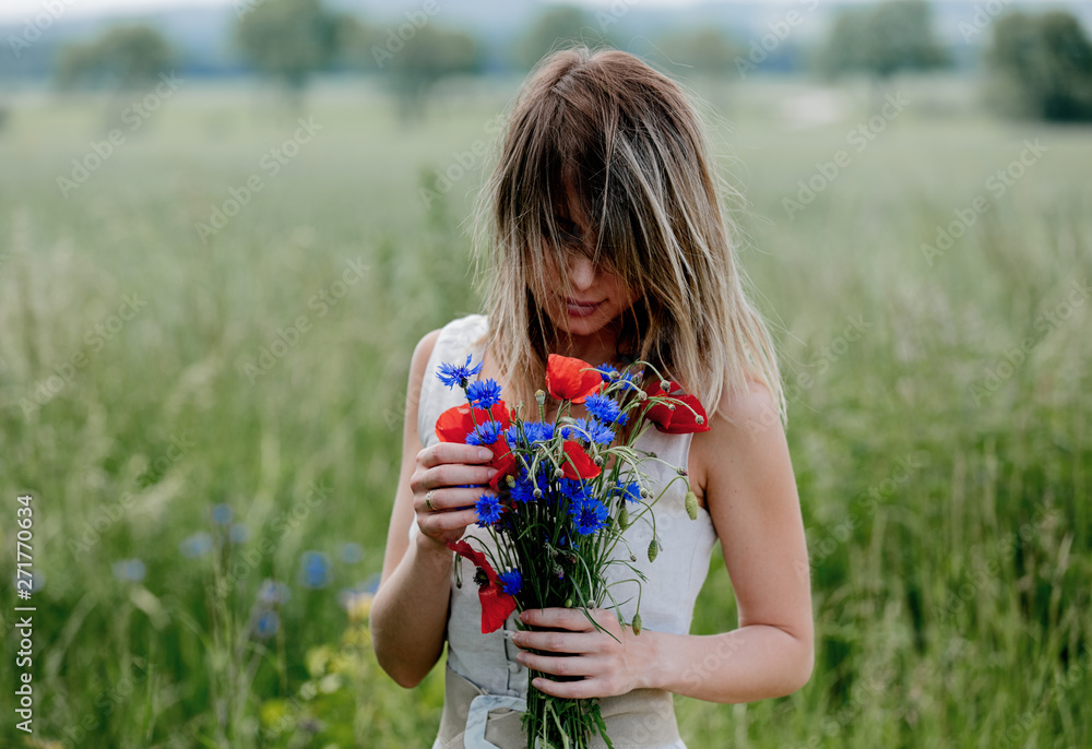 Young woman in dress stay near field with bouquet of Centaurea and Poppy flowers Young woman in dress stay near field with bouquet of Centaurea and Poppy flowers