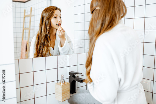 Portrait of a beautiful young woman applying cosmetics on her face while looking at the mirror in the bathroom