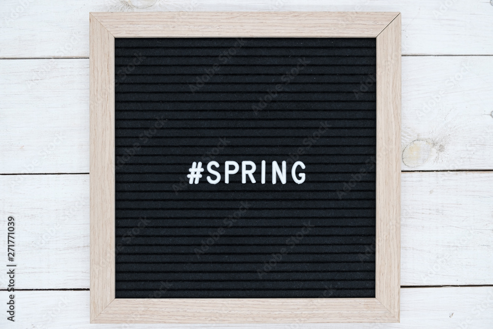 black felt Board with hashtag and word spring in English on white wooden background