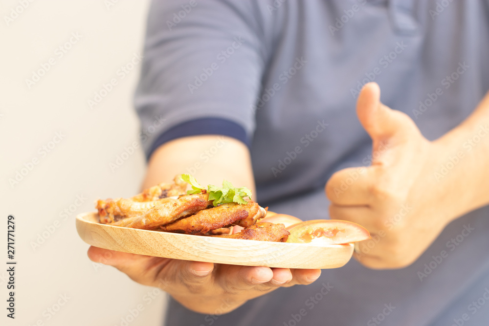 The delivery staff is holding a dish with fried chicken wings to serve to customers in the restaurant. Good quality products that are fresh and safe. Online food order concept.