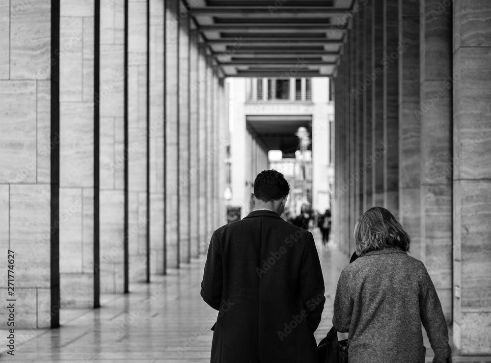 An adult couple walk together though a classical European city. The picture is black and white An adult couple walk together though a classical European city. The picture is black and white