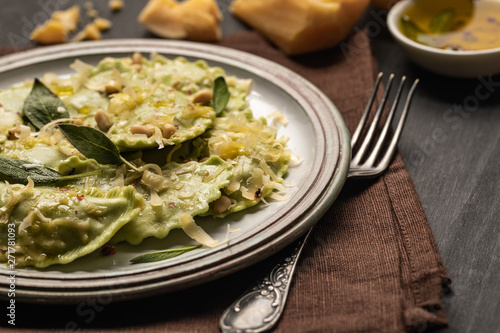 close up view of green ravioli with melted cheese, pine nuts and green sage leaves in retro plate on napkin with fork