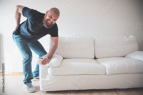 Obraz na plátně Man having backache (low back pain) while moving or trying to lift a sofa