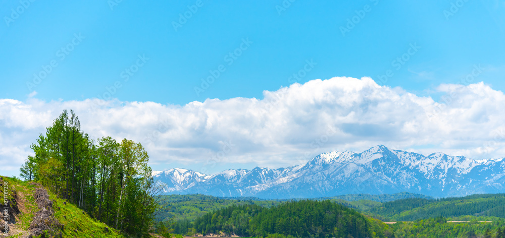 Panoramic rural landscape with mountains. Vast blue sky and white clouds over farmland field in a beautiful sunny day in springtime.