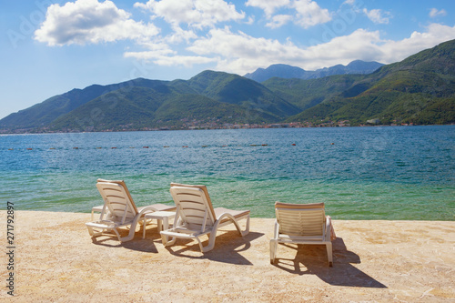 Summer vacation. Beautiful sunny landscape with three chaise lounges on beach. Montenegro, Adriatic Sea, view of Bay of Kotor near Tivat city