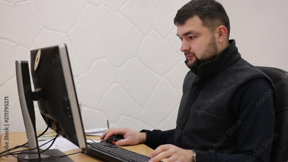 Young bearded office worker man working behind desk on computer.